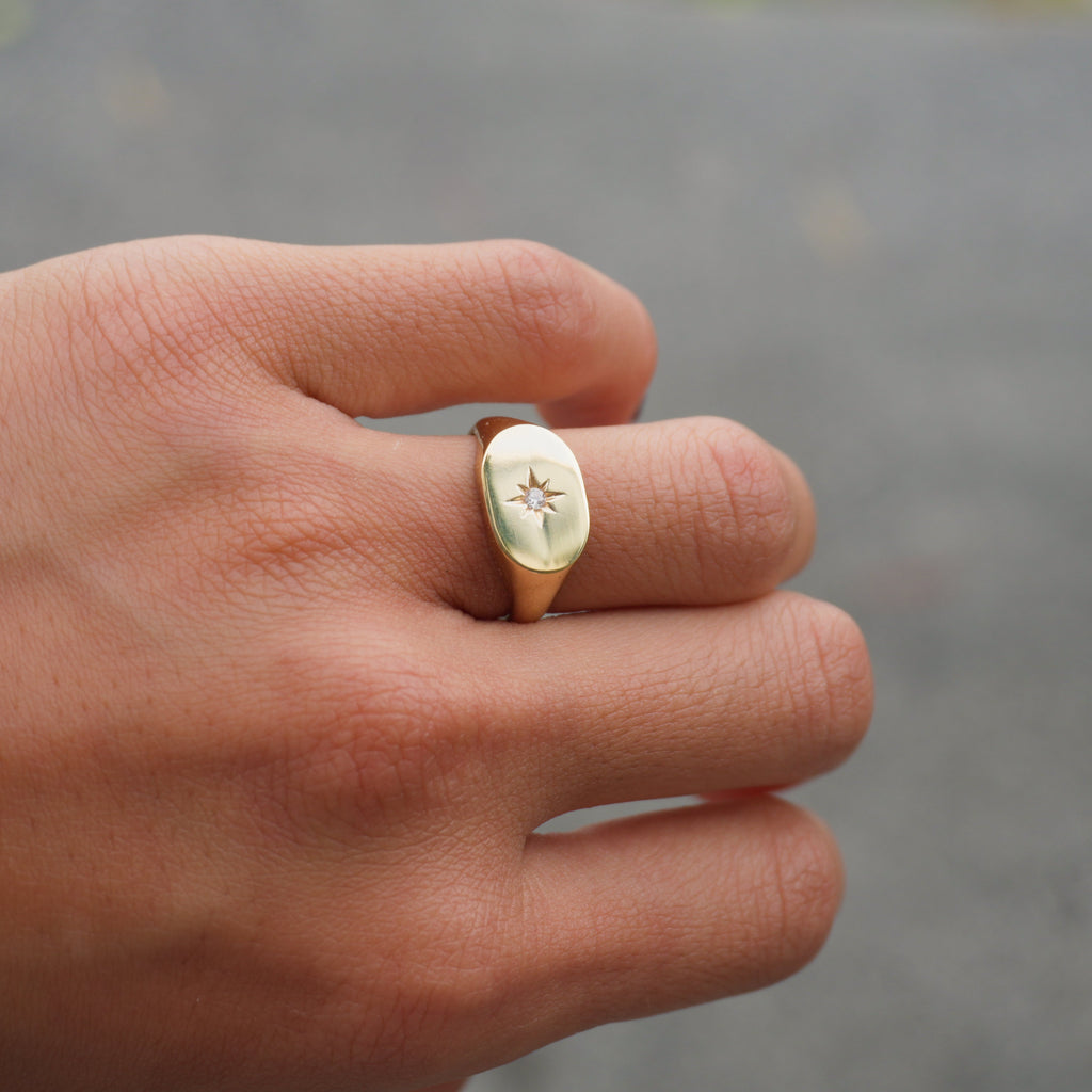 Hand wearing a gold ring with a diamond on a blurred background