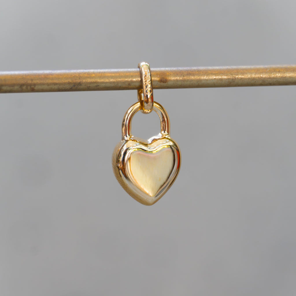 Gold heart-shaped lock pendant on a thin rod against a blurred background