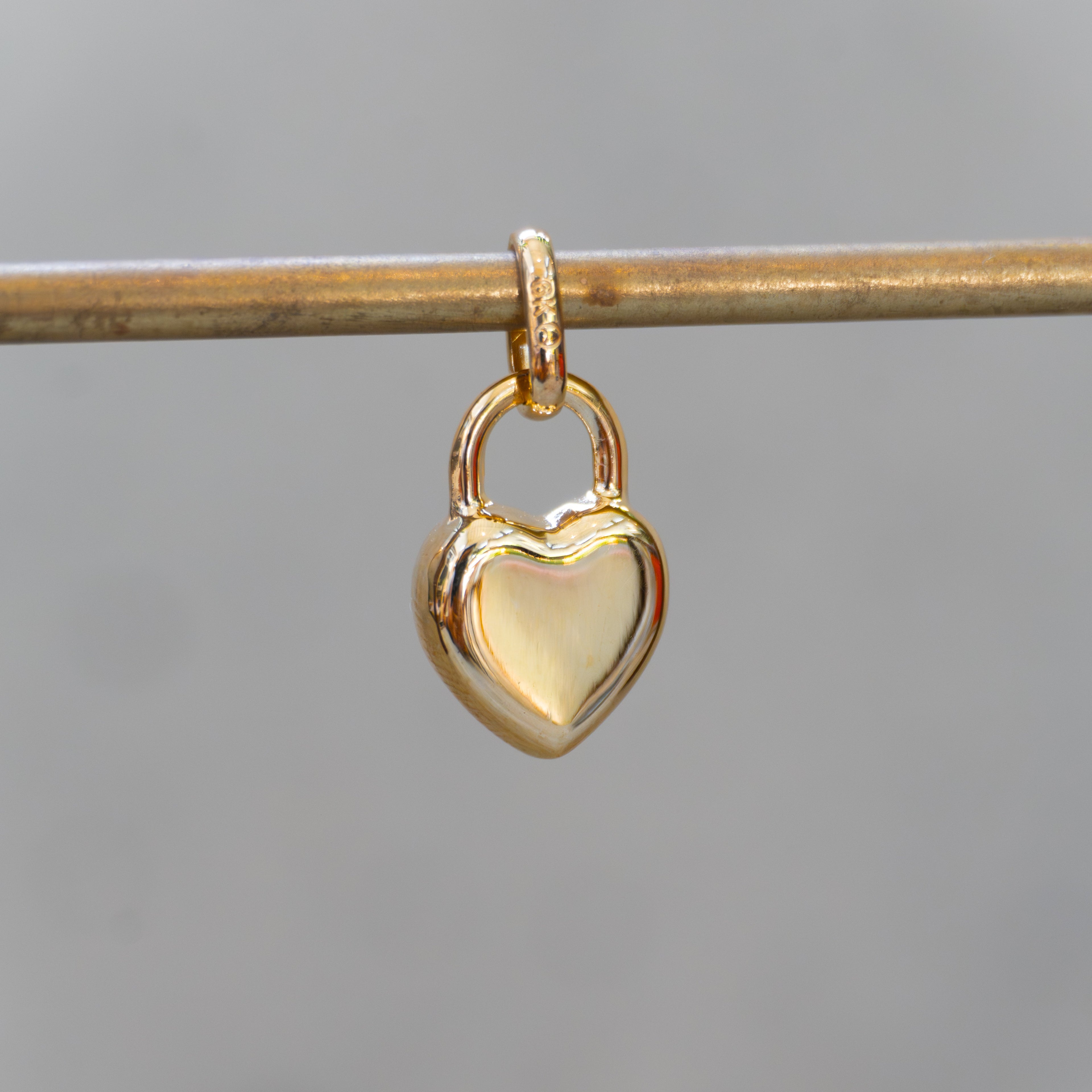 Gold heart-shaped lock pendant on a thin rod against a blurred background