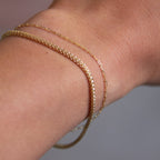 Close-up of a wrist wearing two gold bracelets on a neutral background