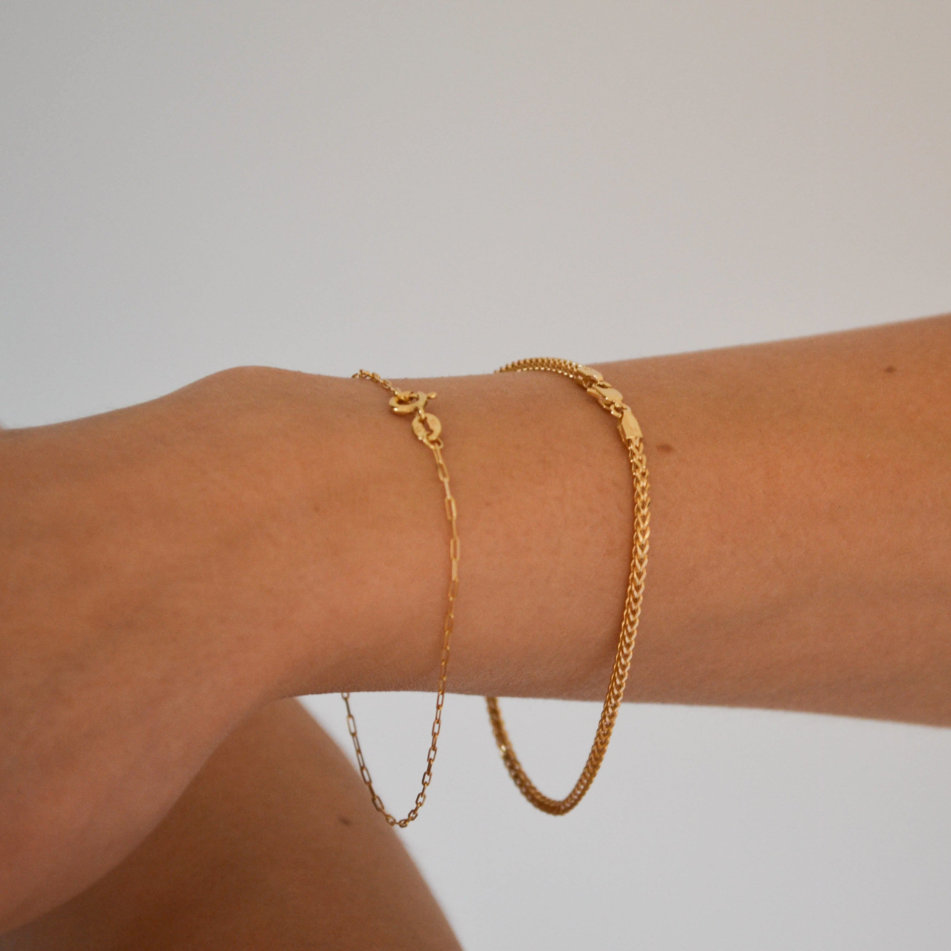 Gold bracelet on a wrist against a plain background